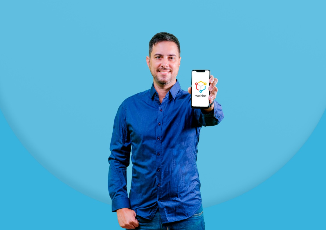 Foto do influenciador Fernando Floripa com uma blusa azul e segurando um celular aberto com a logo da Machine na tela.