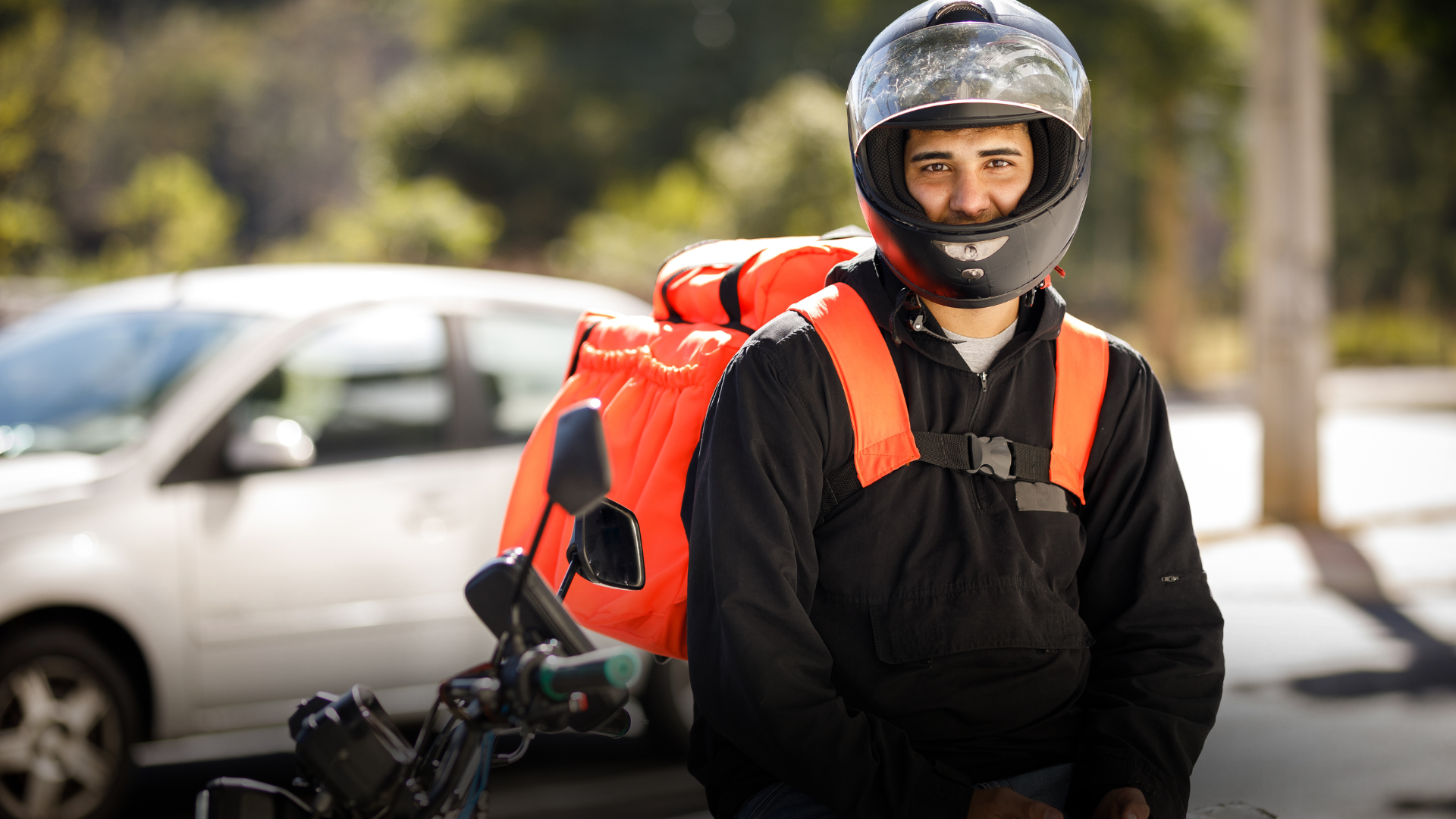 Motoboy com casaco preto e capacete preto, está com uma bag laranja.
