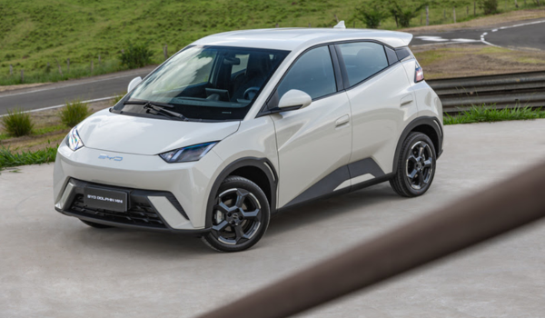 BYD Dolphin Mini, um veículo elétrico compacto com design moderno e aerodinâmico, exibido em uma área ao ar livre. O carro é branco, com detalhes em preto e rodas esportivas.