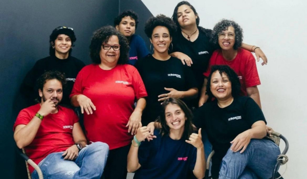 Uma foto de grupo de nove pessoas sorridentes vestindo camisetas com logotipos que parecem ser de uma empresa chamada 'SEÑORITAS'. Quatro delas estão usando camisetas vermelhas e cinco em camisetas pretas. Algumas estão fazendo gestos de 'joinha' e 'paz e amor', transmitindo uma atmosfera positiva e de equipe.
