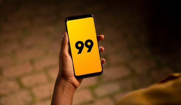 Mão segurando um smartphone com tela voltada para a câmera, exibindo um fundo amarelo com o número 99 em preto no centro da tela