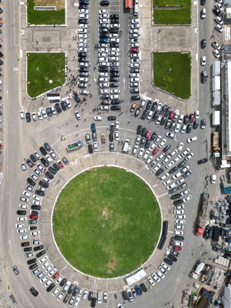 "Vista aérea de um estacionamento circular, com carros estacionados em fileiras que irradiam a partir de um círculo de grama no centro."