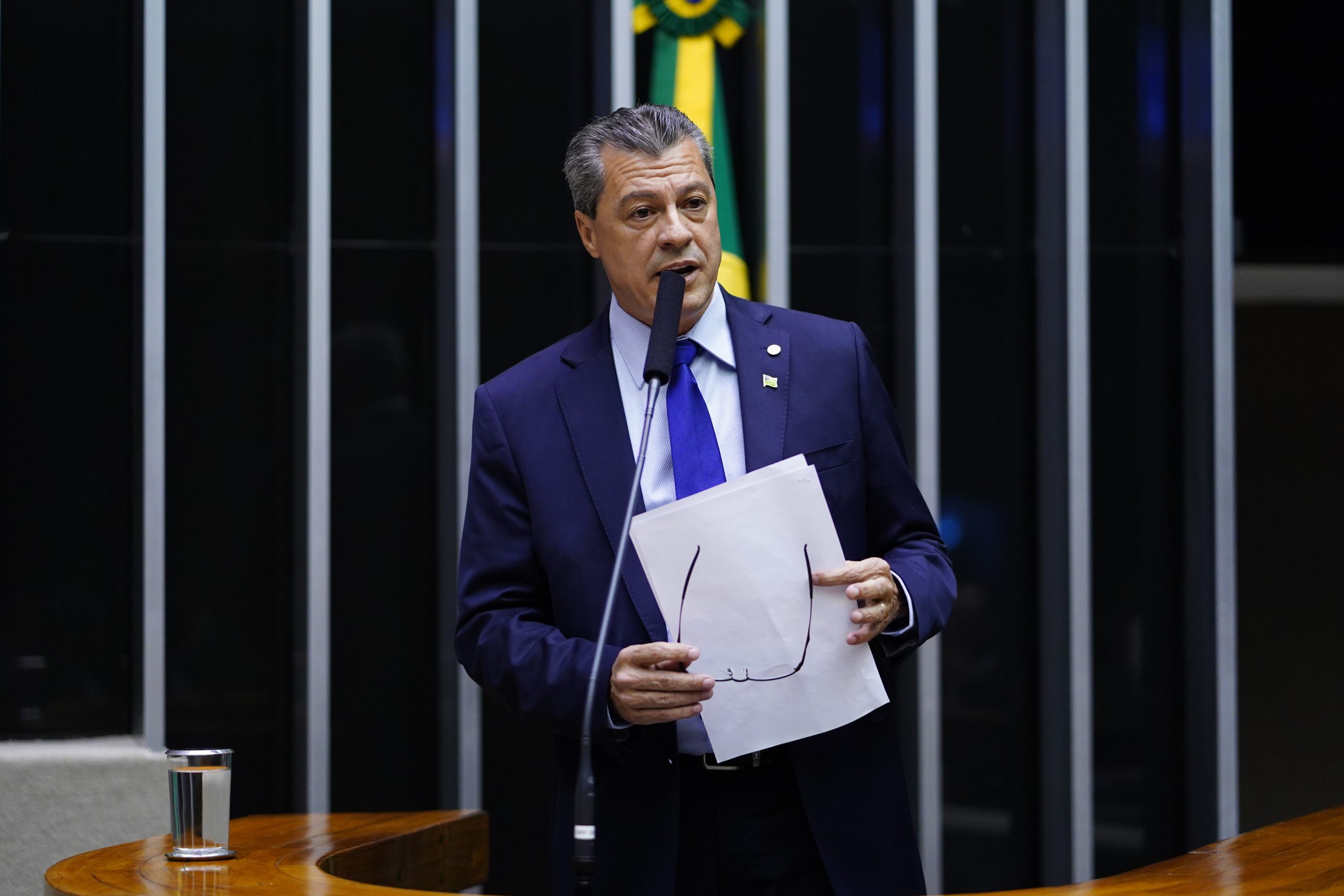 Deputado federal segurando documentos enquanto discursa na Câmara dos Deputados.
