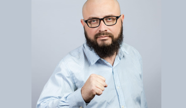 Homem careca, com barba e de óculos posa para foto.