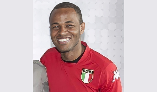 Homem negro sorridente com pouco cabelo e vestido uma camiseta vermelha.