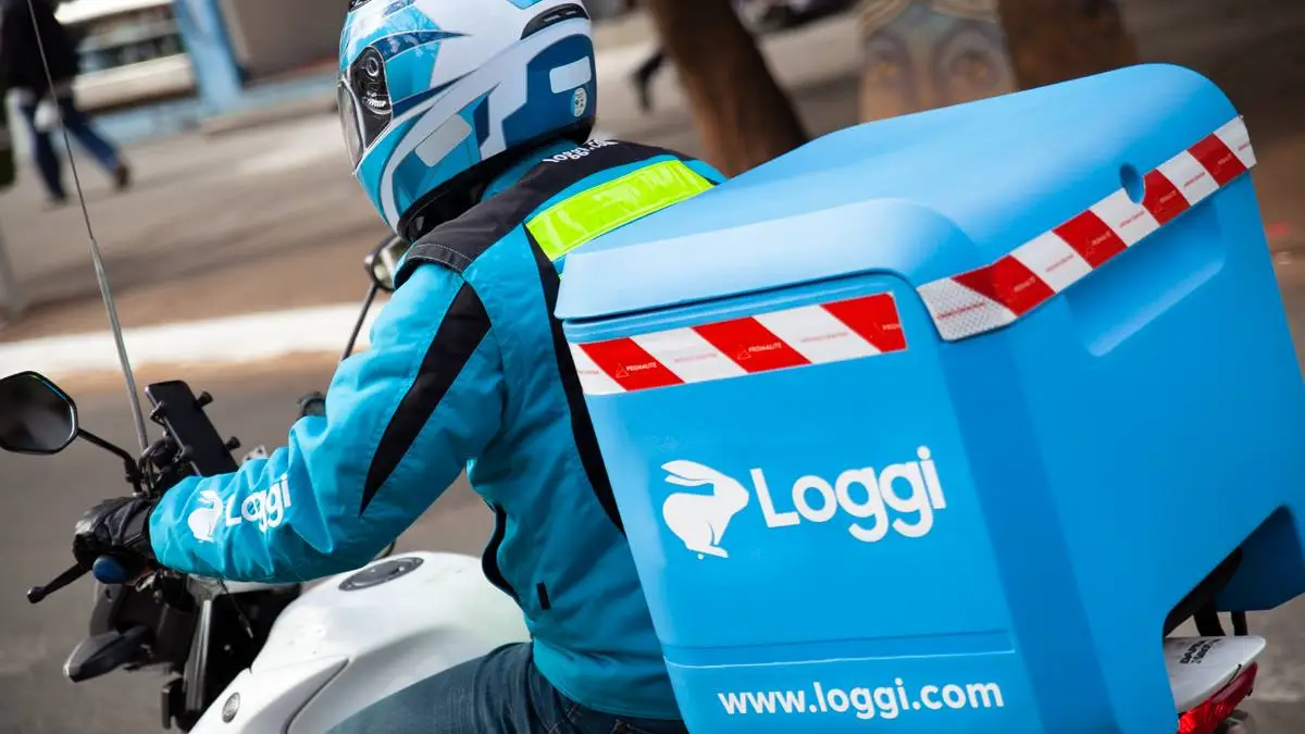 Motociclista da Loggi em ação, utilizando uma motocicleta equipada com um baú azul personalizado para entregas. O entregador veste uniforme e capacete que seguem o padrão de segurança exigido pela empresa, destacando o compromisso da Loggi com a segurança e a eficiência nas entregas urbanas. A Loggi é uma das principais empresas de logística e transporte no Brasil, oferecendo serviços rápidos e confiáveis para diversos tipos de entregas.