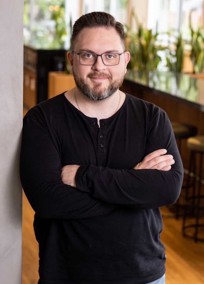 Bruno Rossini, Diretor de Comunicação, em ambiente corporativo, com os braços cruzados e expressão amigável