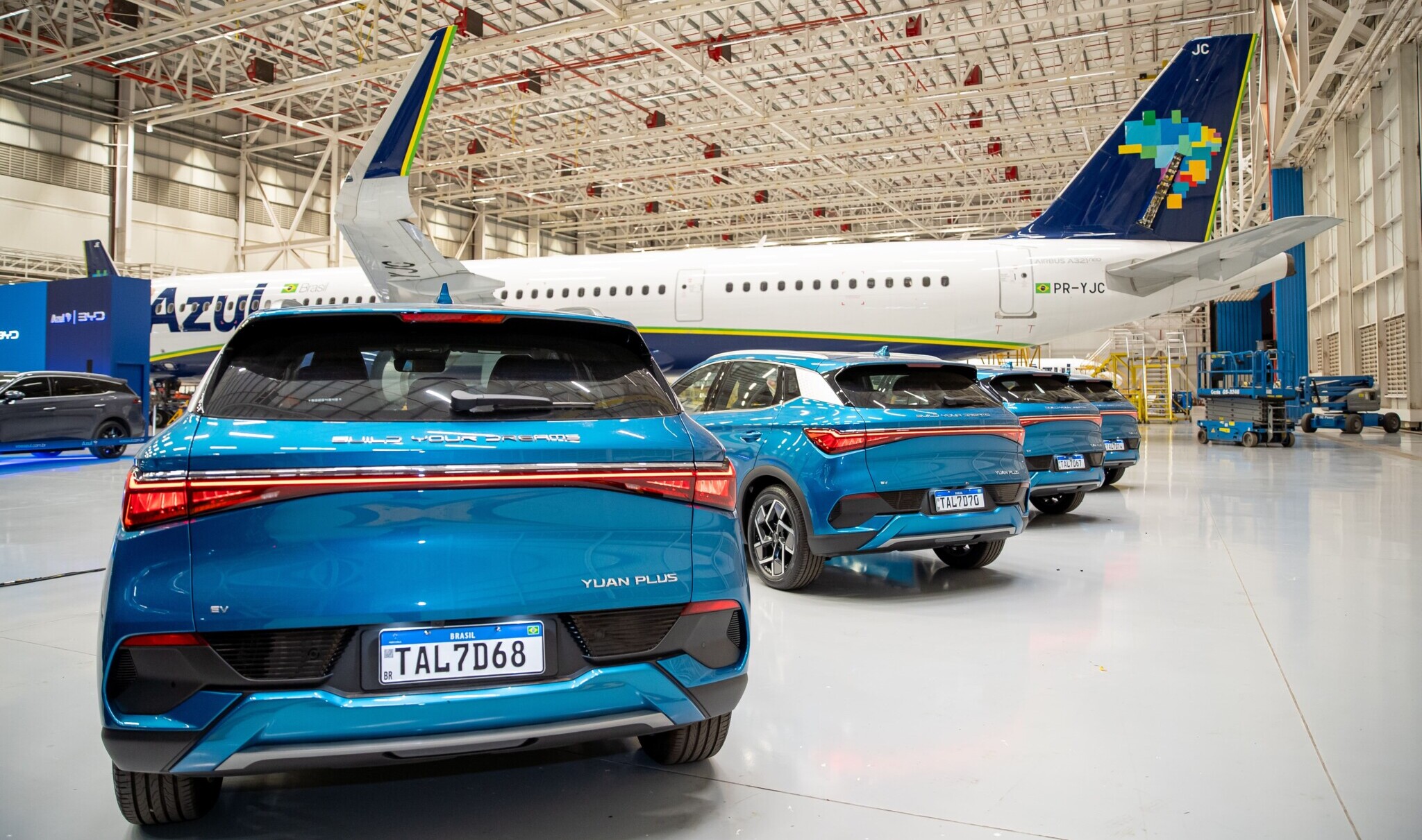 "Carros elétricos BYD Yuan Plus estacionados em hangar ao lado de avião da Azul Linhas Aéreas."