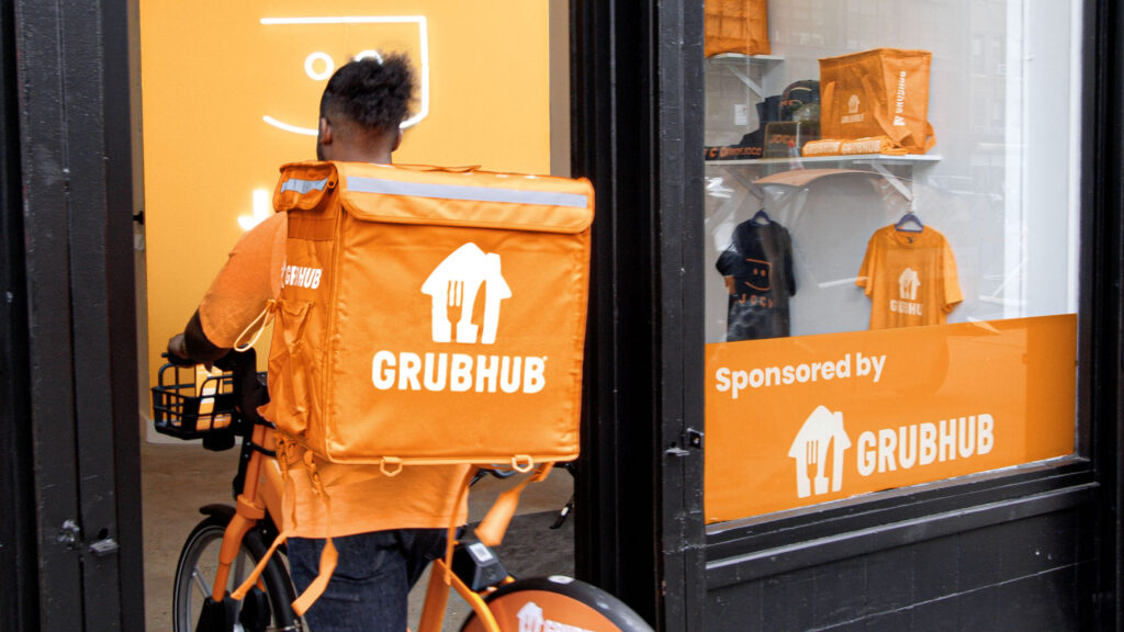 Entregador da Grubhub entrando em loja de bicicletas com mochila laranja.