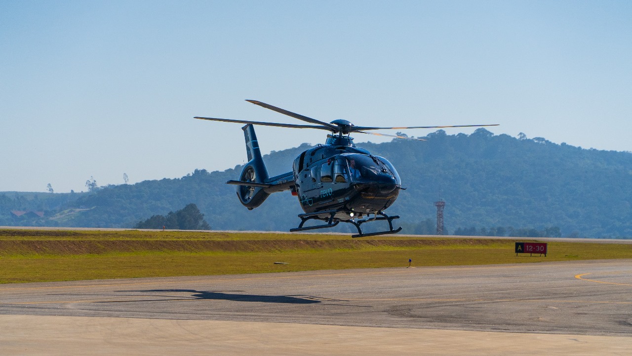 Helicóptero pousando em pista com montanhas ao fundo