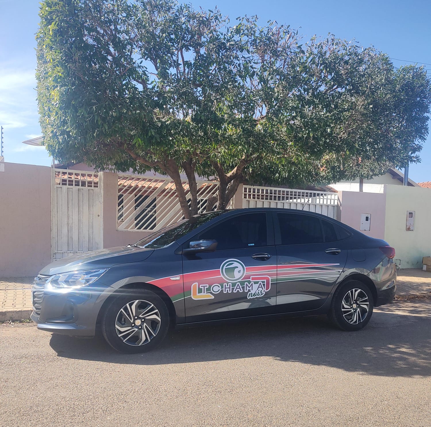 "Carro de aplicativo com adesivo 'Chama Nóiz' estacionado em rua residencial."