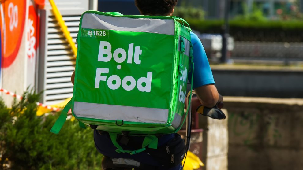 Entregador de Bolt Food de bicicleta em área urbana.