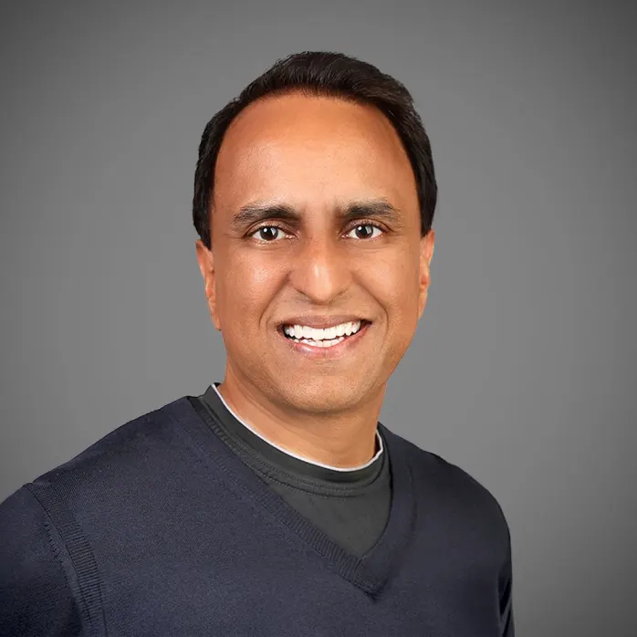 Sundeep Jain sorrindo para a câmera com fundo cinza