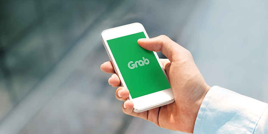 "Mão segurando smartphone com logo do aplicativo Grab na tela"