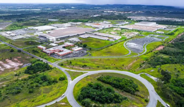 Visão aérea de uma ampla fábrica cercada por vegetação e áreas verdes.