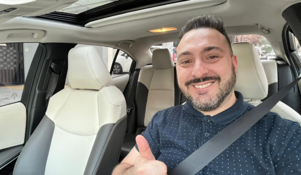 Homem sorridente em um carro, fazendo sinal de positivo com o polegar.