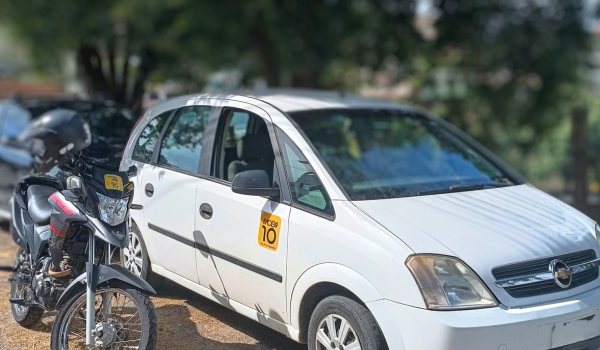 "Carro e moto com adesivos de identificação em um estacionamento arborizado, representando motoristas de aplicativos."