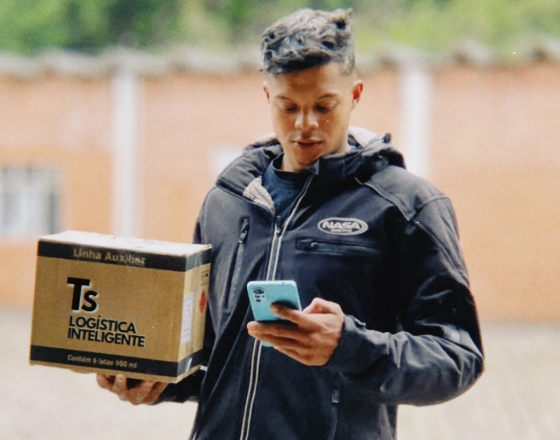 Homem segurando uma caixa e utilizando um celular.