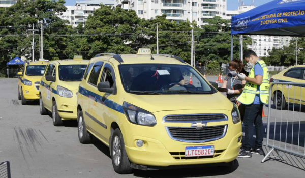 Táxis amarelos enfileirados em uma rua no Rio de Janeiro, com um agente da prefeitura ao lado de um dos veículos verificando documentos.
