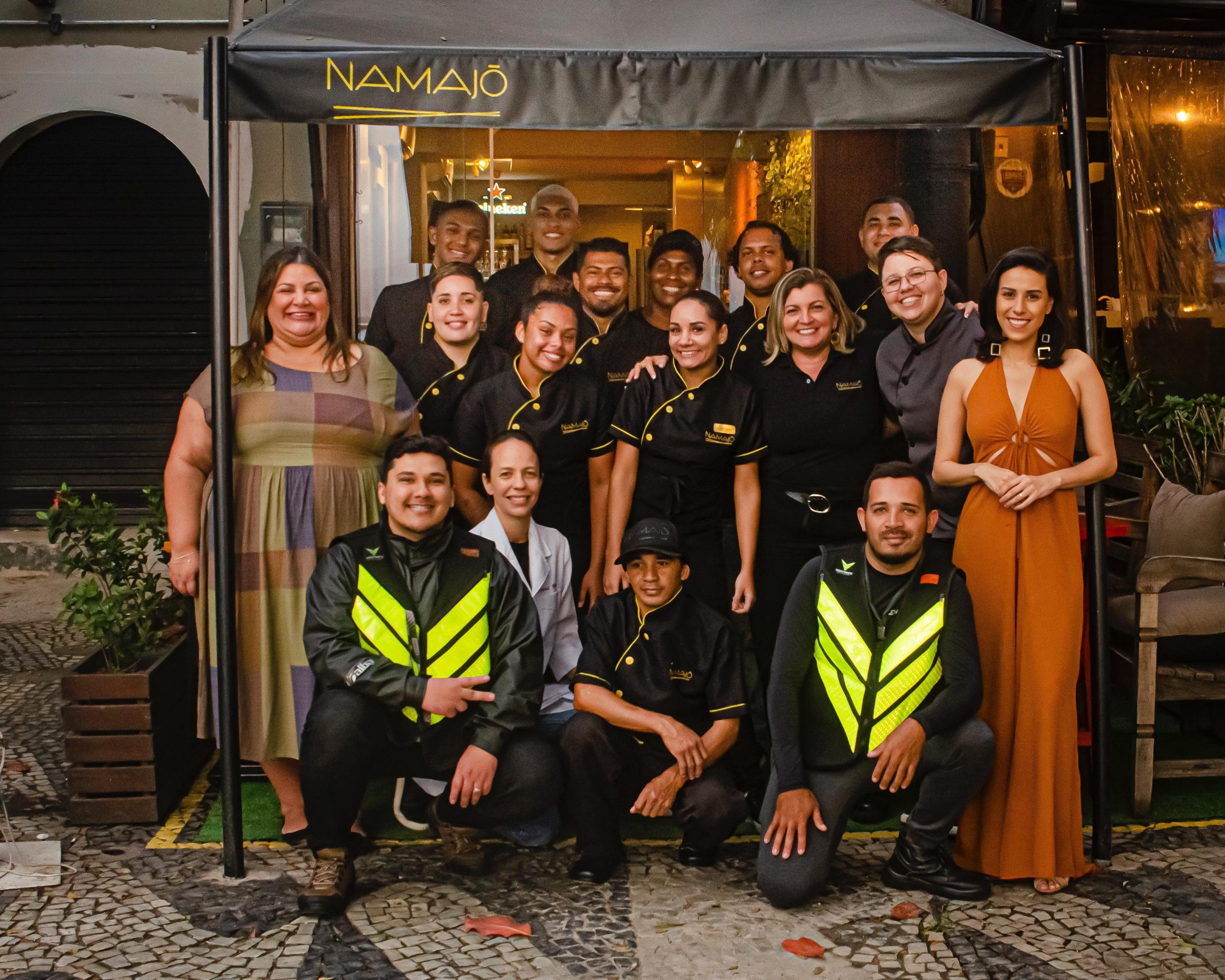 Equipe de funcionários e colaboradores reunidos em frente ao restaurante Namajó, com uniforme característico e coletes de entrega.