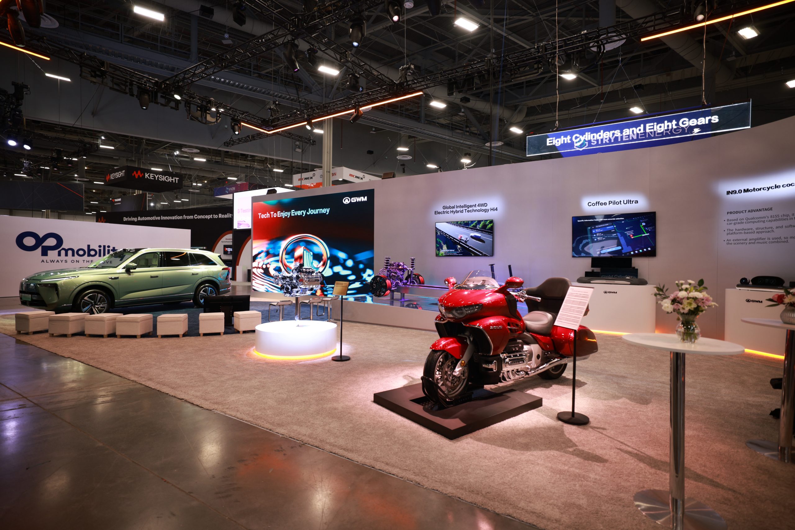 Exposição de tecnologias automotivas em um estande na CES com um SUV verde, uma motocicleta vermelha e telas destacando inovações tecnológicas.