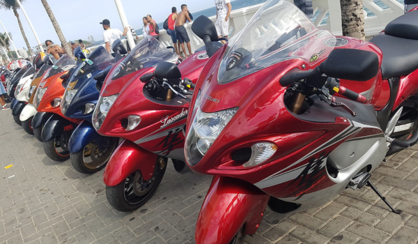 Fileira de motocicletas esportivas estacionadas em um calçadão à beira-mar, com destaque para uma Suzuki Hayabusa vermelha na frente.