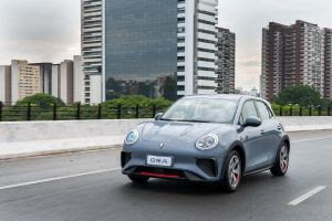 Carro compacto GWM ORA em movimento em uma via urbana, com prédios ao fundo.