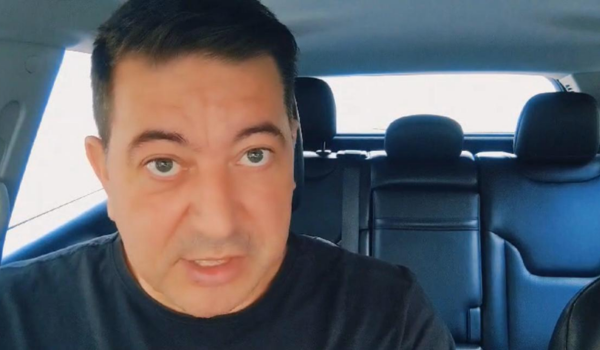 Homem de camiseta preta dentro de um carro, olhando diretamente para a câmera com uma expressão séria