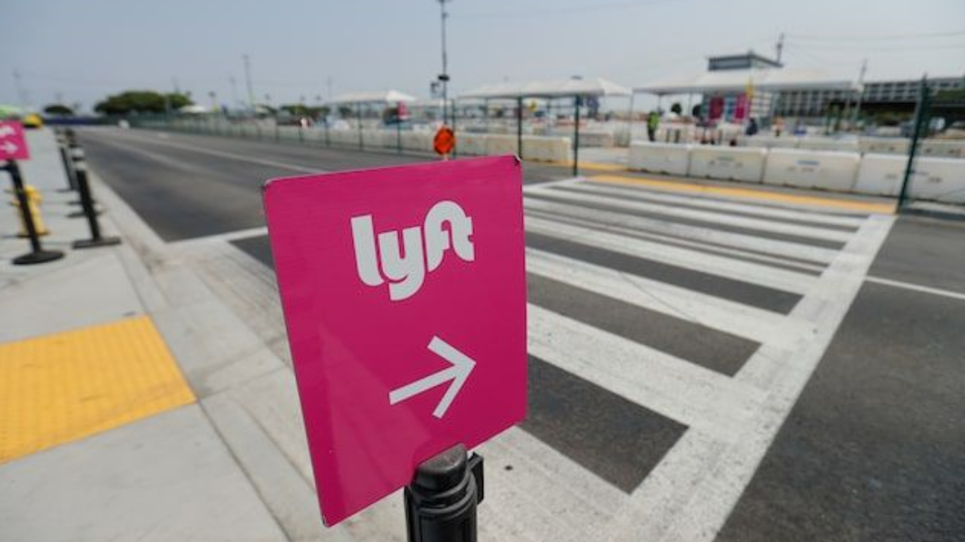Placa rosa da Lyft com seta apontando para a direita, posicionada em frente a uma faixa de pedestres em área urbana.