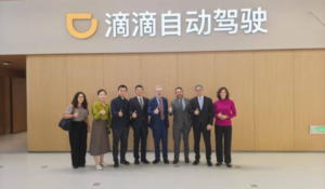 Grupo de oito pessoas posando para foto em frente a uma parede com o logotipo e o nome da empresa Didi em chinês.