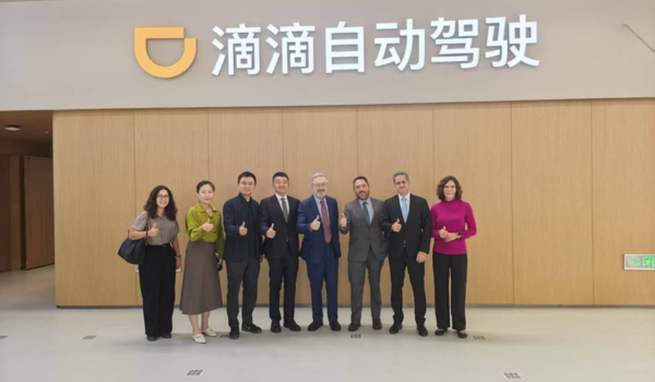 Grupo de oito pessoas posando para foto em frente a uma parede com o logotipo e o nome da empresa Didi em chinês.