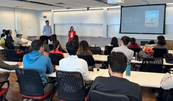 Auditório com pessoas sentadas assistindo a uma apresentação de duas pessoas em frente a um projetor.