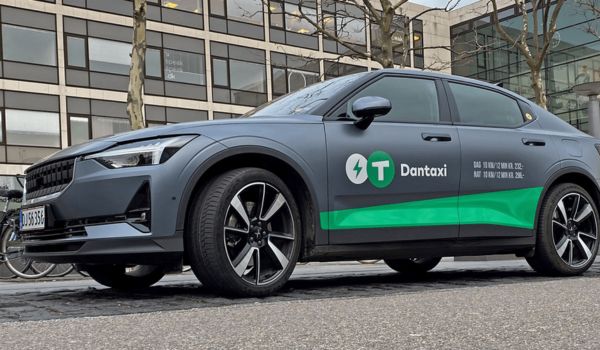 Carro elétrico da Dantaxi estacionado em uma rua urbana, com a identidade visual da empresa em destaque na lateral do veículo.