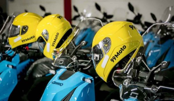 Capacetes amarelos da 99Moto posicionados sobre motos azuis estacionadas em fileira.