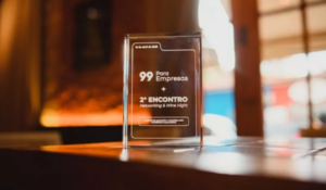 Placa acrílica sobre mesa de madeira com os dizeres “99 Para Empresas – 2º Encontro Networking & Wine Night”, em ambiente interno com iluminação aconchegante.