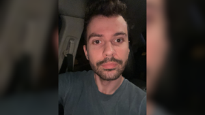 Homem de barba curta e cabelo castanho escuro tira selfie noturna dentro de um carro, com iluminação frontal suave.