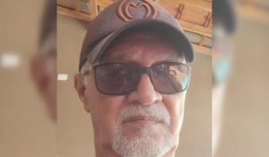 Homem de óculos escuros e boné com logotipo da marca Kibon, em ambiente coberto com telhado de madeira.