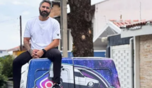 Homem sentado no topo de uma van com uma pintura colorida, representando uma versão estilizada do carro "DeLorean" da série "De Volta para o Futuro", com um design futurista e a presença de uma logo do Instagram. Ele usa uma camiseta branca e calças pretas, com um semblante sério e olhar direcionado à câmera. O fundo mostra uma rua residencial.
