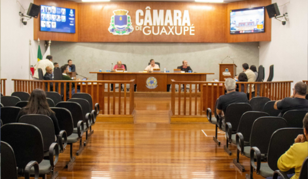 Sessão da Câmara Municipal de Guaxupé com vereadores sentados à mesa diretora e público presente nas cadeiras do plenário.