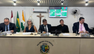 Sessão na Câmara Municipal de Palmeira dos Índios com vereadores sentados à mesa diretora e painel eletrônico ao fundo exibindo votação.