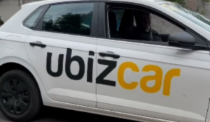 Carro branco com a logomarca da UbizCar estampada na lateral, com motorista visível ao volante.