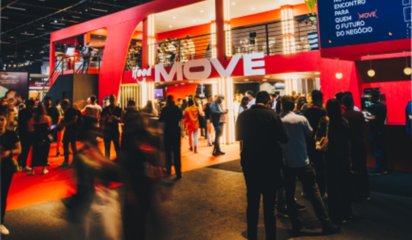 Pessoas circulam e conversam em frente ao estande do iFood MOVE, em um evento movimentado com iluminação vermelha e atmosfera moderna.