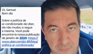 Homem com cabelo escuro e curto, usando uma camiseta de gola polo azul, olhando diretamente para a câmera. Ele está dentro de um carro e há algumas janelas e outros carros visíveis ao fundo. No canto da imagem, há um balão de texto com uma mensagem sobre a política de ar-condicionado da Uber.