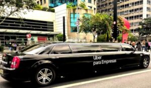 Limusine preta estacionada na Avenida Paulista, em São Paulo, com a frase “Uber para Empresas” escrita na lateral. Ao fundo, pessoas caminham na calçada em frente a edifícios comerciais.
