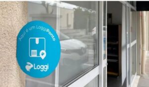 Placa azul da Loggi identifica um ponto de coleta LoggiPonto em fachada de comércio com porta de vidro.