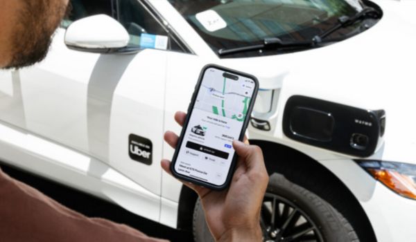 Pessoa segurando um celular com o aplicativo da Uber aberto, em frente a um carro branco elétrico da empresa.