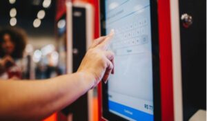 Pessoa interagindo com uma tela sensível ao toque em um terminal eletrônico.