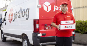 Entregador da Jadlog segurando encomenda em caixa em frente a carro da empresa.