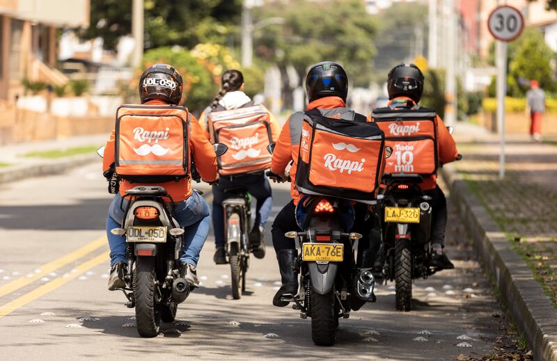 Quatro entregadores de aplicativo dirigindo motos, usando a bag com logo da Rappi.