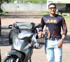 Homem, Robson Pantoja, entregador da Juma Entregas, sorrindo ao lado de uma moto.